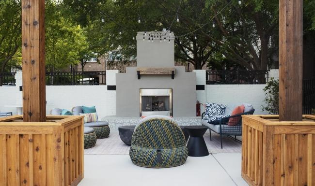 an outside lounge area with chairs, tables and a fireplace
